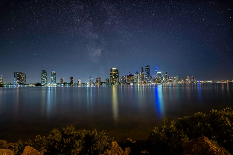 Miami skyline at night under a star-filled sky reflected in the bay