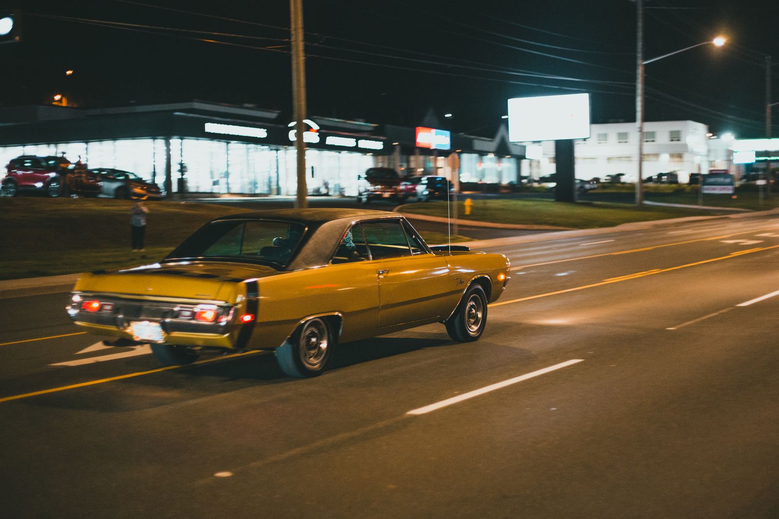 A classic vintage coupe driving down a well-lit city street at night