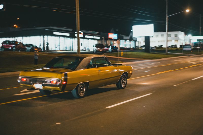 A classic vintage coupe driving down a well-lit city street at night